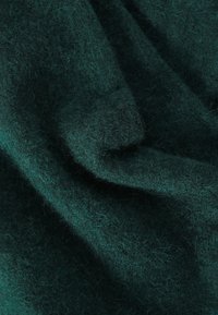 Tumedate roheline villane kangas pehme, tekstuuriga pinnaga ja veidi uduste joontega, näidates voolavaid voldid ja peeneid sügavuse erinevusi.