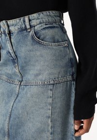 Trapericna suknja svijetlo plave boje s uskim strukom, vidljivim šavovima i detaljima prednjih džepova. Tekstura izgleda glatko s blagim izbljeđivanjem.