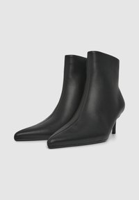 Stivali alla caviglia in pelle nera con punta appuntita, design minimalista, texture liscia e tacco sottile. Cuciture decorative lungo le cuciture.