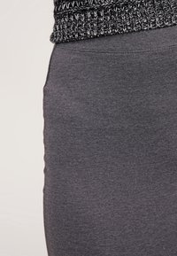 Jupe en jersey gris à la texture lisse, avec une coupe ajustée et une ceinture en tricot noir et blanc. Sans motifs apparents ni éléments métalliques.