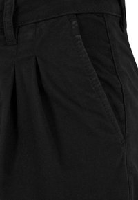 Gros plan d'un pantalon noir montrant une poche latérale, une couture, une boucle de ceinture et la texture du tissu.
