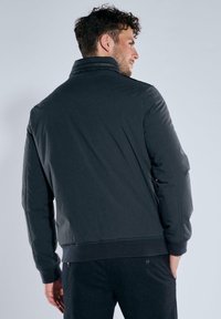Schwarze isolierte Jacke mit hohem Kragen und gerippten Bündchen. Glatte Textur mit körpernahem Schnitt, ausgestattet mit Reißverschluss und ohne sichtbare Logos.
