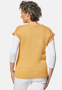 Gebreide trui in felgeel, met korte mouwen, geribbelde zoom, textuurstof, gedragen over een wit langom-shirt, met een casual pasvorm.