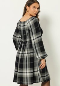 Mustat ja valkoiset ruudulliset mekko, jossa on smockattu yläosa, pitkät puffihihat ja liehuva helma, pehmeästä ja teksturoidusta kankaasta.