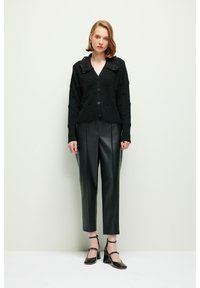 Svart stickad cardigan med ett strukturerat mönster, stor krage och knäppning fram. Kombination med högmidjade svarta läderbyxor och klackar.