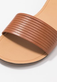 Ruske kožne sandale s trakama koje imaju vodoravne rebra, bež podloga, minimalistički dizajn i ravni đon s crnim rubom.