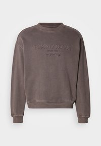 Sudadera marrón con cuello redondo, puños y dobladillo acanalados. Cuenta con el logo bordado "TOMMY JEANS" y una textura suave. Diseño minimalista.