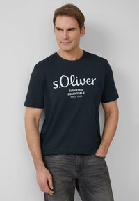 Granatowa koszulka z krótkim rękawem z białym logo "s.Oliver" oraz napisem "ELEVATED ESSENTIALS SINCE 1969". Wykonana z miękkiej bawełny, o luźnym kroju.