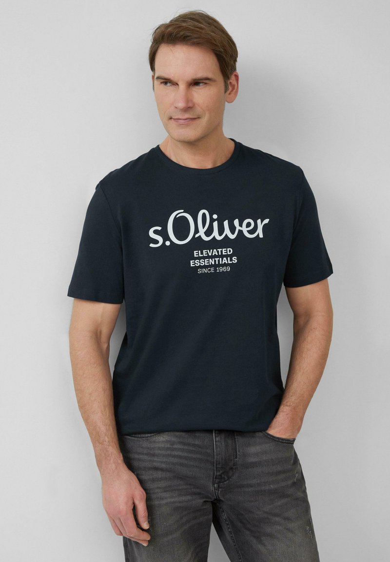 Granatowa koszulka z krótkim rękawem z białym logo "s.Oliver" oraz napisem "ELEVATED ESSENTIALS SINCE 1969". Wykonana z miękkiej bawełny, o luźnym kroju.