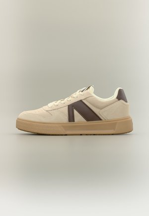 Beżowy niski sneaker z brązowym skórzanym detalem po boku i gumową podeszwą na neutralnym tle.