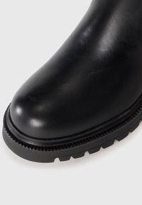 Stivale alla caviglia in pelle nera con punta arrotondata, superficie testurizzata e suola in gomma spessa con motivo a trazione.