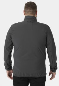 Hombre con chaqueta softshell gris oscuro de espaldas contra un fondo liso, con el cuello levantado y mangas largas.