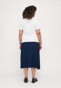 White short-sleeve t-shirt paired with a knee-length navy pleated skirt. The skirt has a flowing texture and a subtle sheen. Black shoes complete the look.
