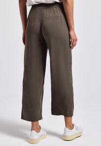 Olive green wide-leg trousers with an elastic waistband, featuring two back pockets and a smooth, lightweight texture. Paired with white sneakers.