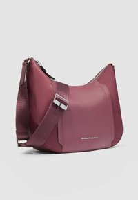 Schultertasche aus burgunderrotem Leder mit glatter Textur, verstellbarem gewebtem Riemen, silberfarbenen Metallakzenten und Reißverschlussverschluss.