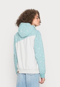 Hoodie azul claro com um padrão texturizado de bolinhas e parte de trás branca sólida. Punhos e bainha elásticos; capuz ajustável com detalhes em metal.