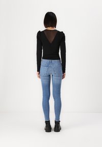 Black long-sleeve top with puff shoulders and sheer back, paired with light blue skinny jeans and black ankle boots.