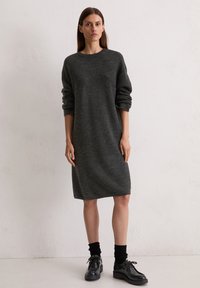 Robe grise en tricot avec une coupe décontractée, des manches longues et un col rond. Associée à des chaussures noires à lacets et des chaussettes noires côtelées.