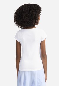 Λευκή ριγέ μπλούζα με κοντά μανίκια και στρογγυλή λαιμόκοψη, με ελαφρώς εφαρμοστή γραμμή, φορεμένη με φούστα σε ανοιχτό μπλε ριγέ.