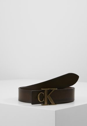 Ciemnobrązowy skórzany pasek zwinięty na białej powierzchni z frontową złotą klamrą z logo „cK”.
