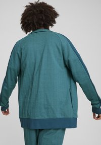 Teal sportjacket med sildbenestruktur, afslappet pasform, ribbede manchetter og et kontrasterende blåt panel langs siderne, designet til komfort.