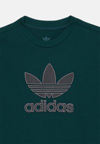 Tumši zaļš kokvilnas T-krekls ar lielu pelēku izšūtu Adidas logotipu un trefoilu dizainu priekšpusē, ar apaļu kakla izgriezumu.