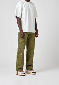 T-shirt blanc en coton à manches courtes associé à un pantalon cargo vert olive avec des coutures diagonales et plusieurs poches, complété par des baskets multicolores.