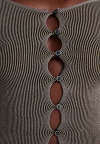Brauner, geripptes Oberteil aus Stoff mit dekorativen runden Ausschnitten und dunklen Knöpfen. Glatte Textur mit tailliertem Design entlang des Ausschnitts und der Vorderseite.