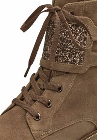 Bottines en suède marron à bout rond, avec un panneau accent en bronze pailleté et des lacets marron passés dans des œillets en métal.