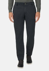 Tmavosivé, slim-fit nohavice vyrobené zo hladkej zmesi bavlny, s gombíkovým zapínaním a detailmi vrecka, v kombinácii s čiernymi teniskami.