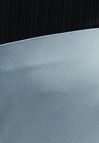 Nærbillede af en glat, buet metalbladskant holdt op mod en mørk, ribbet stofbaggrund.