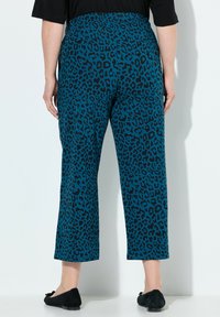 Tropfenblaue Leopardenmuster-Hosen mit entspannter Passform, verkürzter Länge und elastischem Bund. Kombiniert mit schwarzen Ballerinas und einem kurzärmeligen Oberteil.