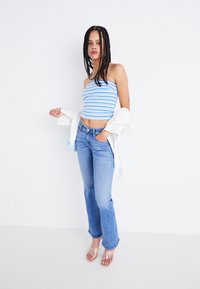 Top sin mangas a rayas azul y blanco con diseño ajustado, combinado con jeans de pernera acampanada de lavado claro y sandalias de tacón transparente.