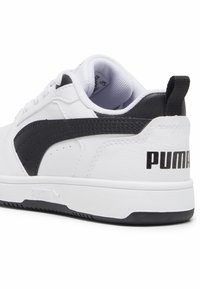 Baskets blanches avec des accents noirs, fabriquées en cuir synthétique lisse. Présentent un bout arrondi, des détails texturés et un logo prominent au talon.