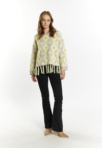 Overmaat gebreide pullover in het grijs met gele geometrische patronen, met een franjerand. Gecombineerd met zwarte flare jeans en tan kleurige haklaarzen.