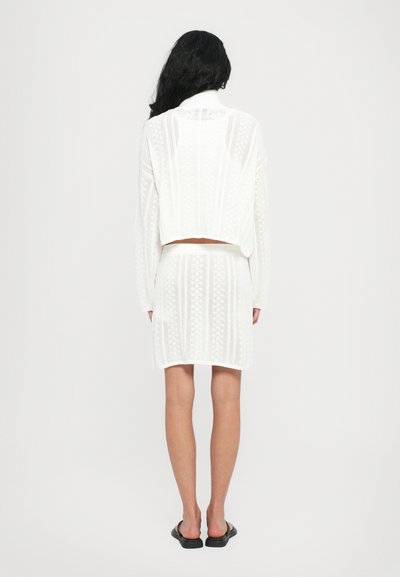 White knit two-piece outfit featuring a cropped top with a textured pattern and a knee-length skirt with a matching design. Sandals visible.