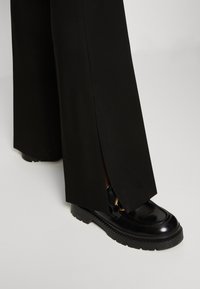 Svarta vida byxor med sidoklackar, parat med blanka svarta loafers med tjock sula och gulddetaljer.