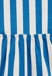 Niebiesko-biała tkanina w paski z marszczonym szwem na dole, charakteryzująca się na przemian grubymi i cienkimi paskami, o miękkiej teksturze.