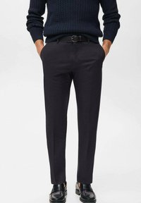 Black tailored trousers with a smooth texture, straight leg design, and a belt. Worn with a dark, textured knitted sweater and black shoes.