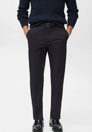 Pantalones ajustados negros con una textura suave, diseño de pierna recta y un cinturón. Llevados con un suéter de punto texturizado oscuro y zapatos negros.