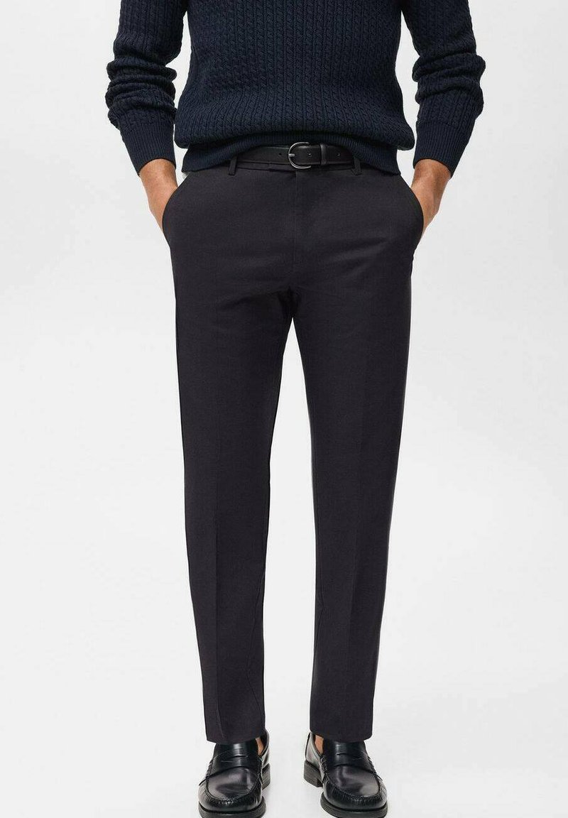 Black tailored trousers with a smooth texture, straight leg design, and a belt. Worn with a dark, textured knitted sweater and black shoes.