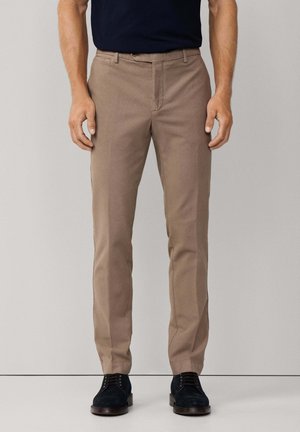 Beige maßgeschneiderte Hose mit glatter Textur, Reißverschluss und Gürtelschlaufen, kombiniert mit dunklen Schuhen. Die Passform ist schlank und mit geradem Bein.