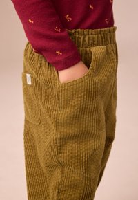 Olijfgroene corduroy broek met een geribbelde textuur, voorzien van zijzakken en een elastische tailleband, gecombineerd met een bordeauxrode top met lange mouwen.
