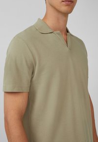 Korte mouwen polo-shirt in licht olijfgroen, met een v-hals en een zachte stof. Gepaste pasvorm met nette stikdetails.
