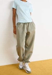 Světle modré bavlněné tričko s krátkým rukávem, zkombinované se světle zelenými tepláky a bílými teniskami s zeleným akcentem.