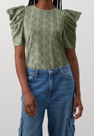 Jasnozielona bluzka z bufiastymi rękawami, o teksturowanym wzorze fal, z okrągłym dekoltem, zestawiona z niebieskimi dżinsami typu cargo. Swobodna i lekka tkanina.