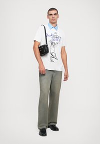 White t-shirt with blue collar, featuring a graphic print. Loose-fitting gray jeans. Black crossbody bag and black shoes complete the look.