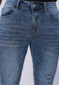Vaqueros de denim azul claro con un acabado desgastado, que cuentan con un bolsillo frontal, cinturas para el cinturón y parches desgastados en las rodillas.