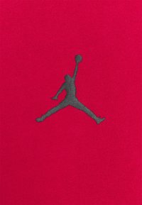 Silhouette d’un joueur de basket sautant avec un bras tendu vers le haut tenant un ballon sur un fond de tissu rouge.