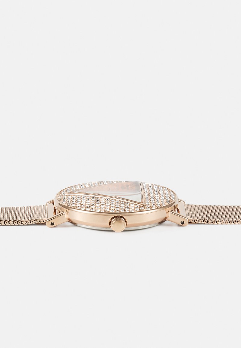 Montre en or rose avec un cadran rond, ornée de cristaux dans un motif triangulaire, dotée d'un bracelet en maille et d'une couronne latérale pour les réglages.